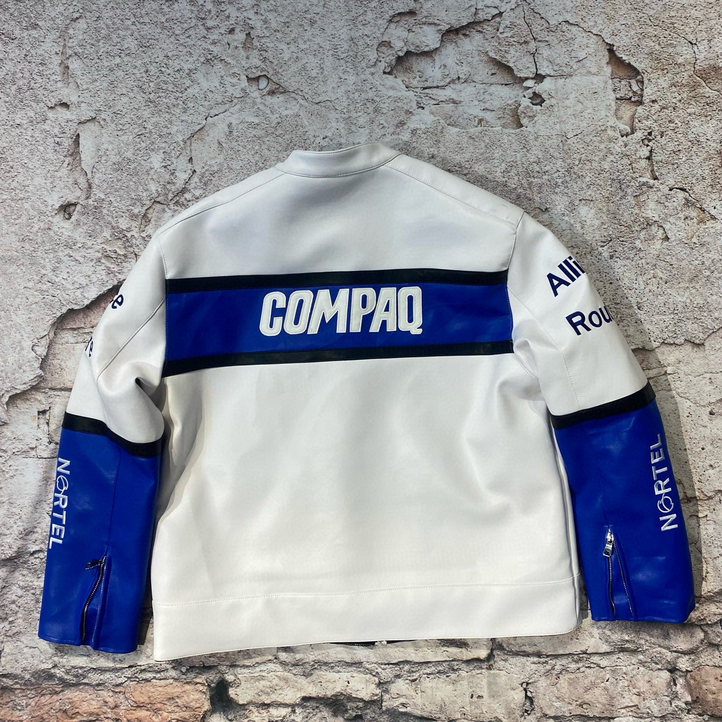White sweatshirt with blue accents and visible branding on a textured stone wall.