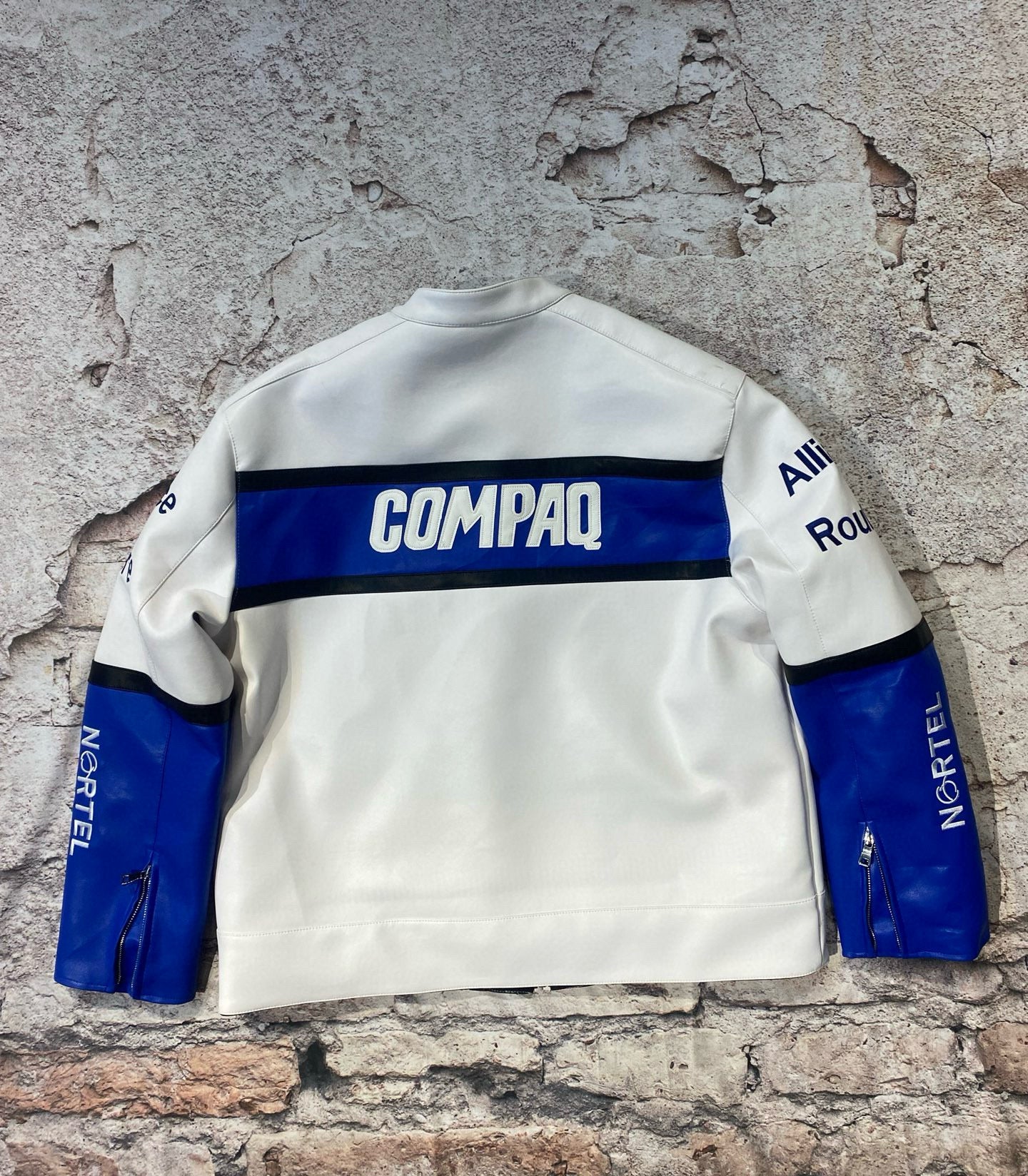White sweatshirt with blue accents and visible branding on a textured stone wall.