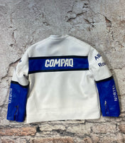 White sweatshirt with blue accents and visible branding on a textured stone wall.
