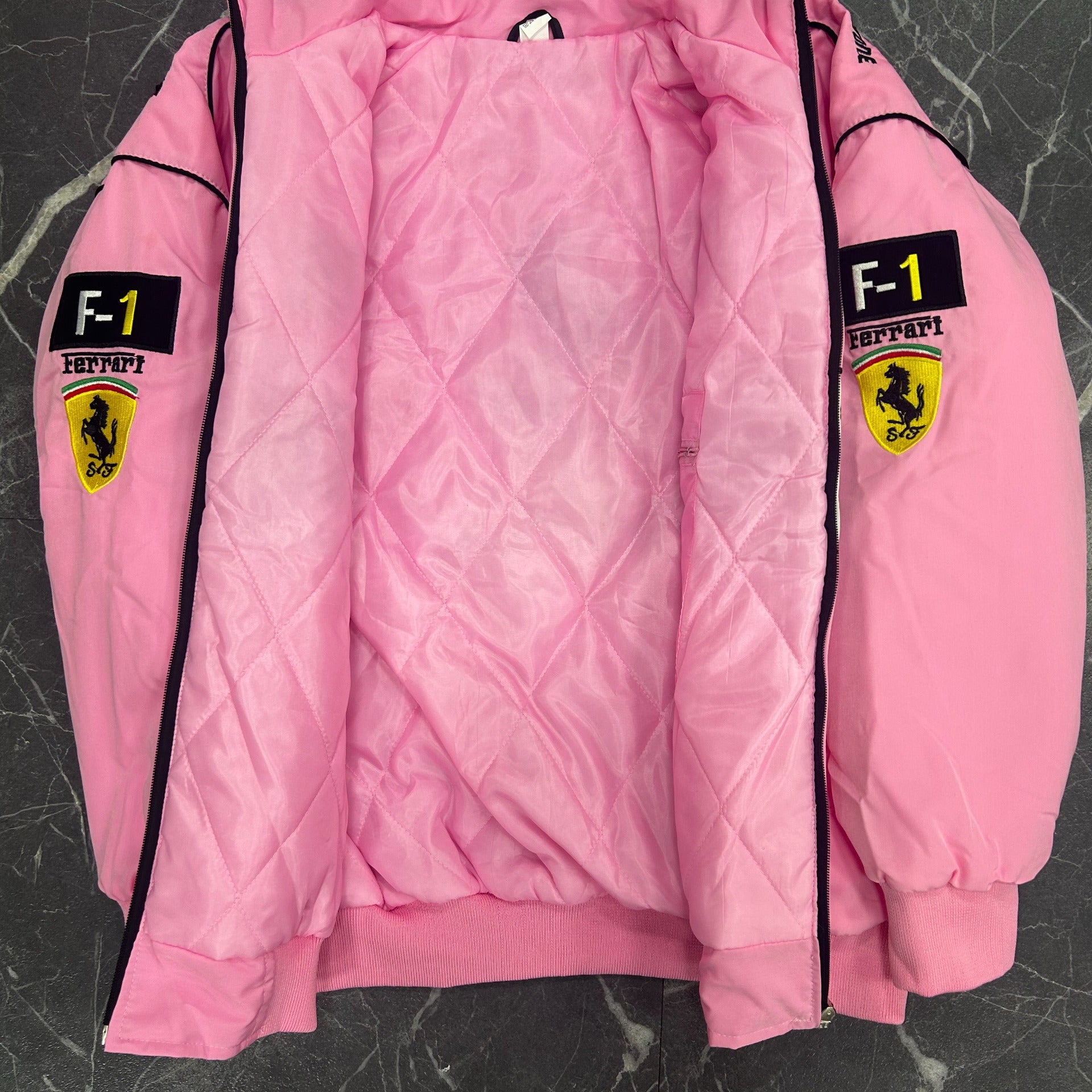 Pink quilted jacket with Ferrari logos on a dark textured surface