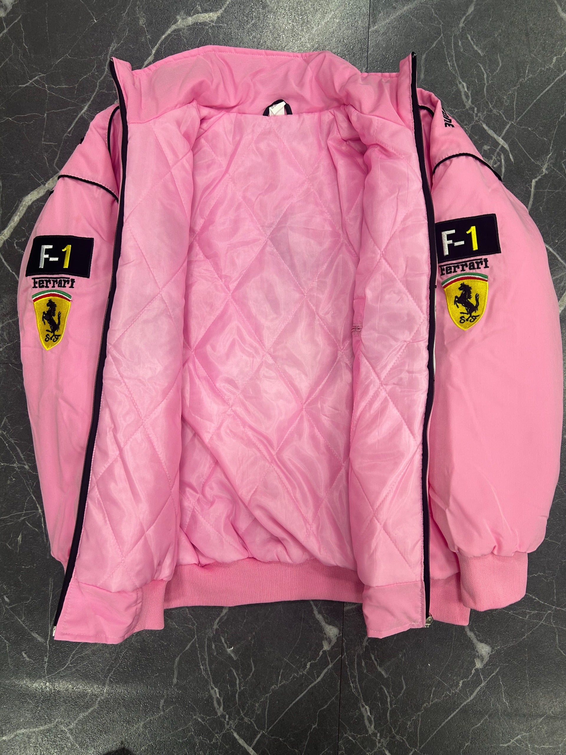 Pink quilted jacket with Ferrari logos on a dark textured surface