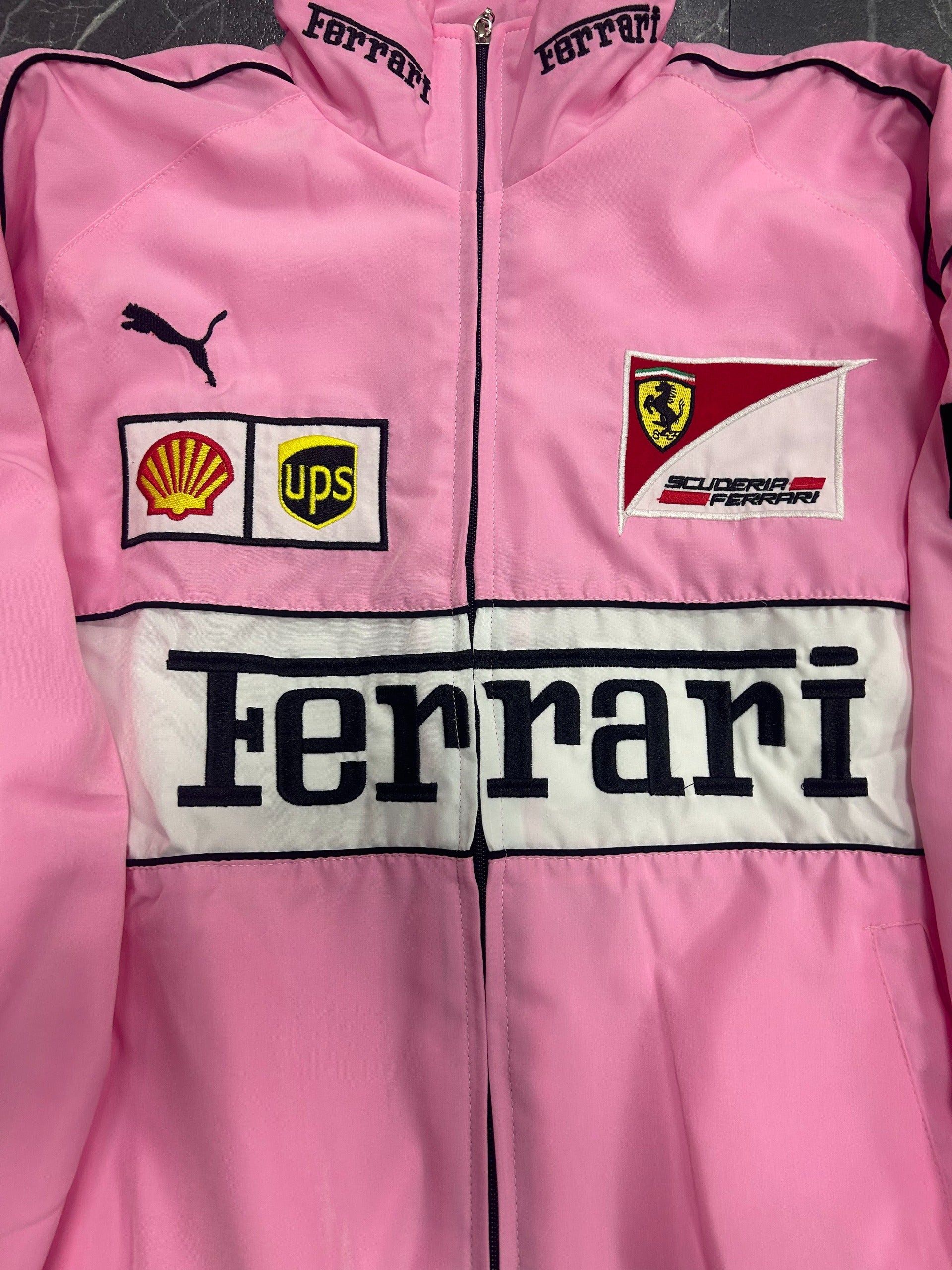 Pink jacket with Ferrari, Puma, UPS, and Shell logos on a checkered background
