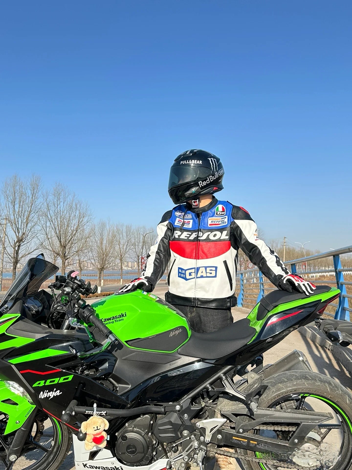 Person in racing gear sitting on a green motorcycle with a clear blue sky background